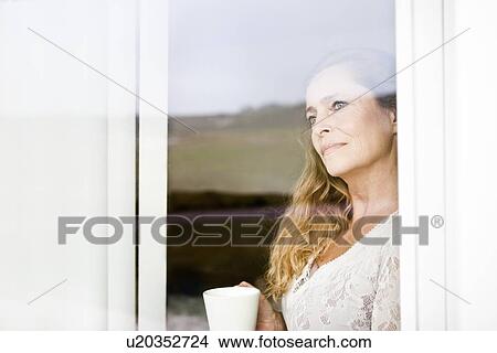 Woman having cup of coffee at window View Large Photo Image Picture - Woman having cup of coffee at window. Fotosearch