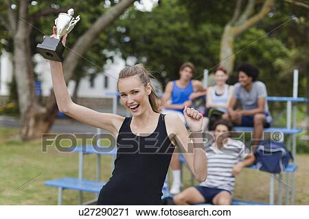 Stock Image - Woman holding trophy in park. Fotosearch