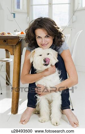 Stock Image - Woman hugging dog in kitchen. Fotosearch