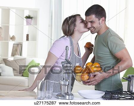 Stock Photo - Woman kissing boyfriend in kitchen. Fotosearch