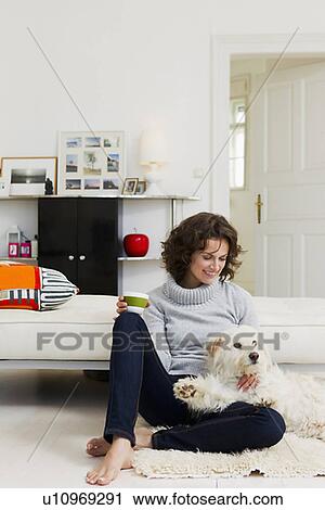 Stock Image - Woman petting dog in living room. Fotosearch