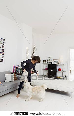 Stock Photo - Woman playing with dog in living room. Fotosearch