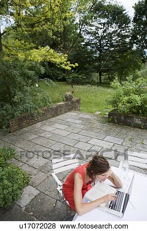 Stock Photo - Woman reading and using laptop outdoors. Fotosearch