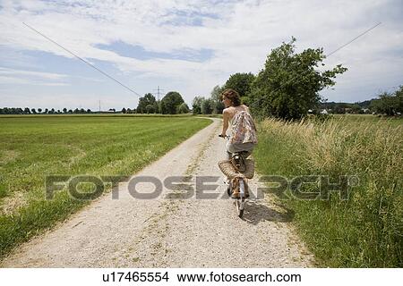 Picture - Woman riding bicycle on rural road. Fotosearch