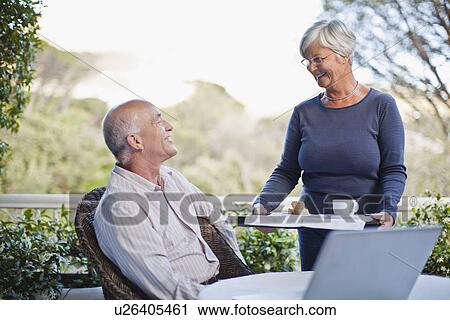 Stock Image - Woman serving husband coffee outdoors. Fotosearch