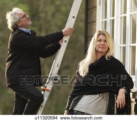 Picture - Woman smiling as husband climbs ladder. Fotosearch