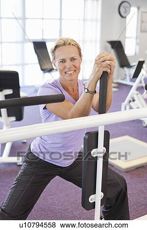 Stock Photo - Woman using weights machine in gym. Fotosearch