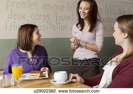 Stock Image - Women talking to waitress in cafe. Fotosearch