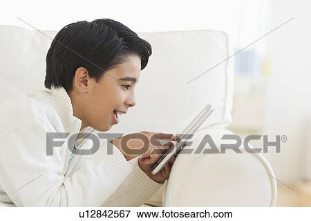 Boy (12-13) using digital tablet on sofa View Large Photo Image Stock Photo - Boy (12-13) using digital tablet on sofa. Fotosearch