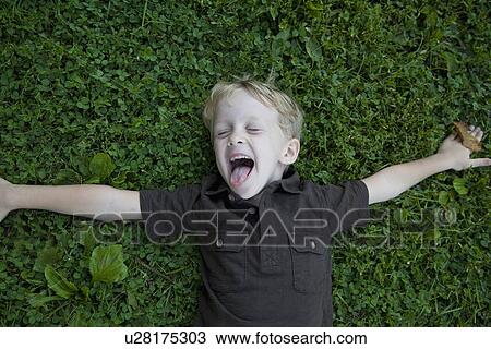 Stock Image - Boy (4-5) lying on lawn laughing. Fotosearch