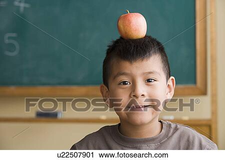 Stock Image - Boy (6-7) with apple on his head. Fotosearch