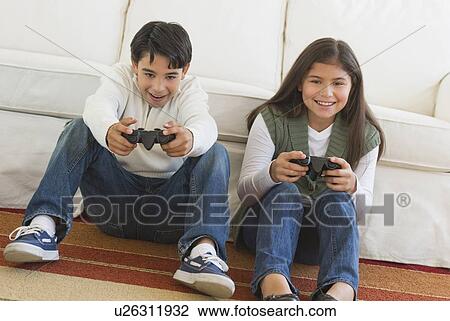 Stock Image - Brother (12-13) and sister (10-11) playing video games. Fotosearch