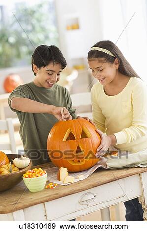 Stock Photo - Brother (12-13) and sister (10-11) doing Jack o lantern. Fotosearch