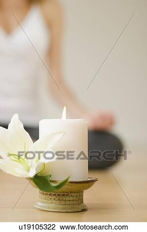 Stock Image - Candle and flower with woman practicing yoga in background, studio shot. Fotosearch