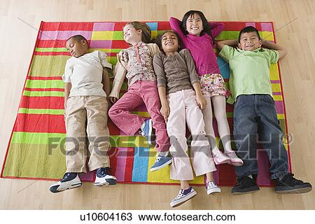 Stock Image - Children (6-7) lying on blanket in classroom. Fotosearch