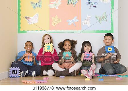 Stock Photo - Children (6-7) sitting and holding letters in classroom. Fotosearch