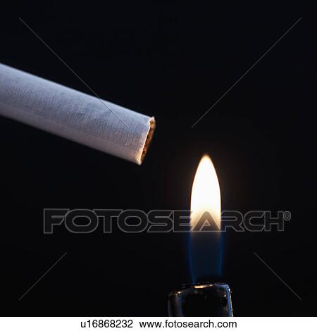 Stock Image - Close up of cigarette and flame from lighter on black background. Fotosearch