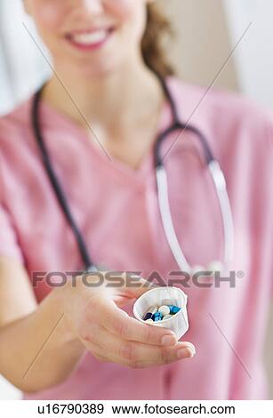 Stock Photo - Close up of female nurse holding cup with pills. Fotosearch