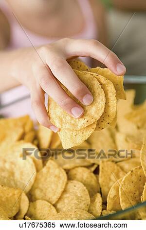 Stock Photography - Close up of girl's (10-11) hand taking potato chips from bowl. Fotosearch