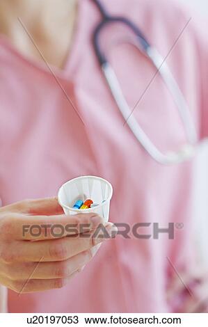 Stock Image - Close up of hand of female nurse holding cup with pills. Fotosearch