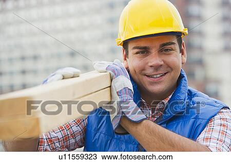Construction worker carrying planks on construction site View Large Photo Image Stock Image - Construction worker carrying planks on construction site. Fotosearch