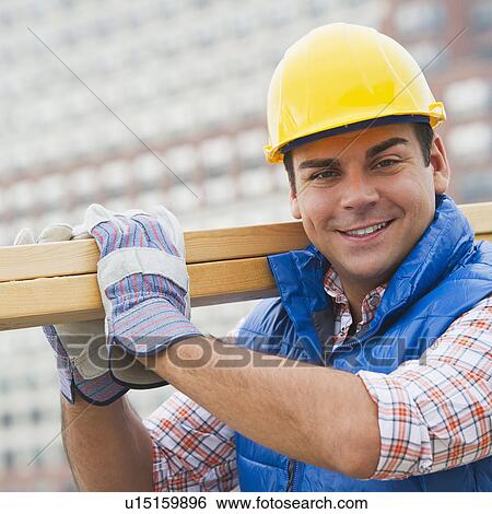 Stock Photograph - Construction worker carrying planks on construction site. Fotosearch
