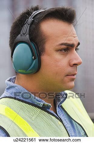 Stock Image - Construction worker wearing reflective clothing and headphones. Fotosearch