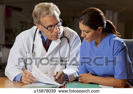 Doctors sitting at desk and reading files View Large Photo Image Stock Photo - Doctors sitting at desk and reading files. Fotosearch