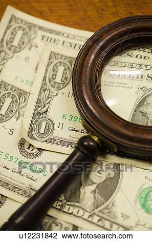 Stock Image - Dollar bills with magnifying glass, studio shot. Fotosearch