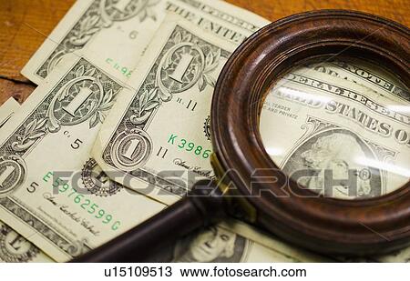 Stock Image - Dollar bills with magnifying glass, studio shot. Fotosearch