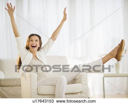 Stock Image - Excited woman sitting in chair at home. Fotosearch
