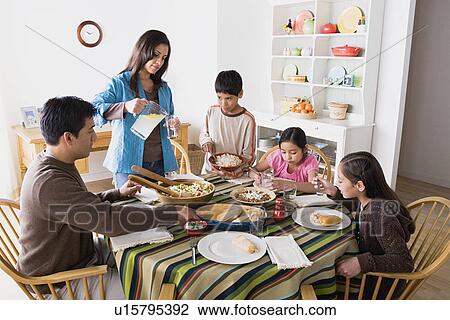 Stock Image - Family with three children (8-9, 10-11) dining together. Fotosearch