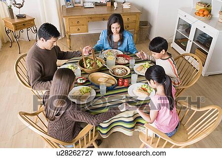 Stock Photo - Family with three children (8-9, 10-11) praying at table before dining. Fotosearch