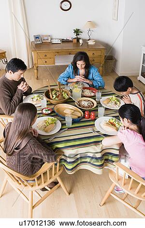 Stock Photograph - Family with three children (8-9, 10-11) praying at table before dining. Fotosearch