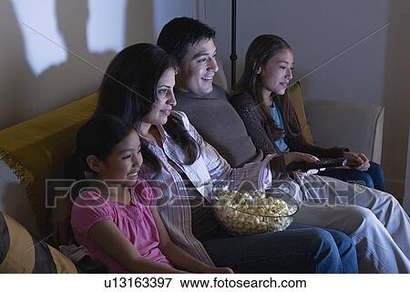 Stock Photo - Family with two children (8-9, 10-11) watching tv on sofa. Fotosearch