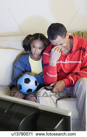 Stock Image - Father and Daughter (10-11) watching sports on tv. Fotosearch