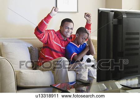 Stock Image - Father and Son (12-13) watching sports on tv. Fotosearch