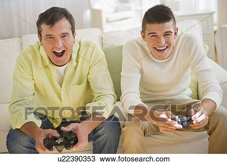 Stock Image - Father and son (16-17) playing video game. Fotosearch
