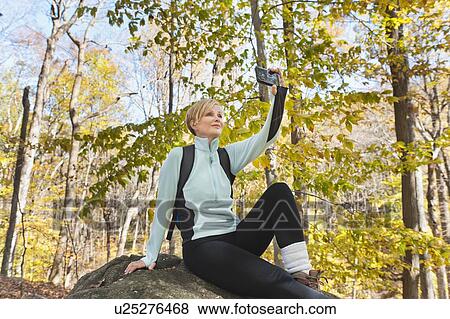 Stock Photo - Female hiker photographing self on rock in forest. Fotosearch
