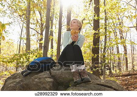 Stock Photo - Female hiker resting on rock in forest. Fotosearch