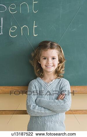 Stock Image - Girl (6-7) in classroom against blackboard. Fotosearch