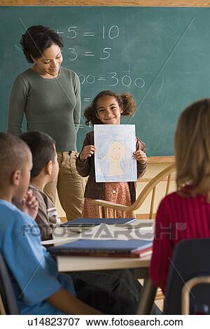 Girl (6-7) showing her drawing in classroom View Large Photo Image Stock Photo - Girl (6-7) showing her drawing in classroom. Fotosearch