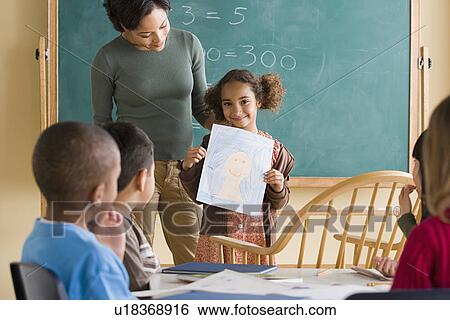 Girl (6-7) showing her drawing in classroom View Large Photo Image Stock Photograph - Girl (6-7) showing her drawing in classroom. Fotosearch