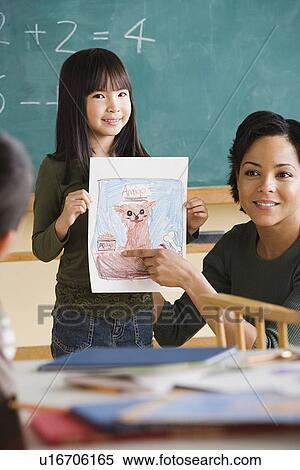 Stock Photography - Girl (6-7) showing her drawing in classroom. Fotosearch