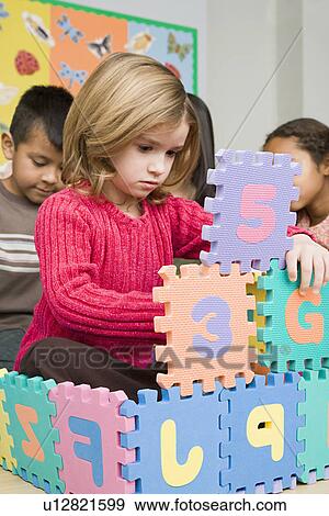 Stock Photo - Girls (6-7) playing with puzzle letters. Fotosearch