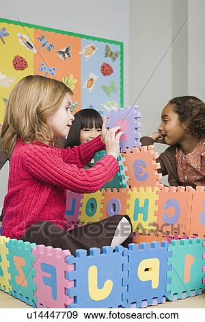 Stock Photo - Girls (6-7) playing with puzzle letters. Fotosearch
