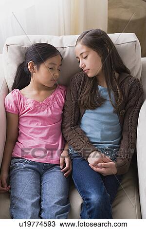 Stock Image - Girls (8-9, 10-11) sleeping in armchair. Fotosearch