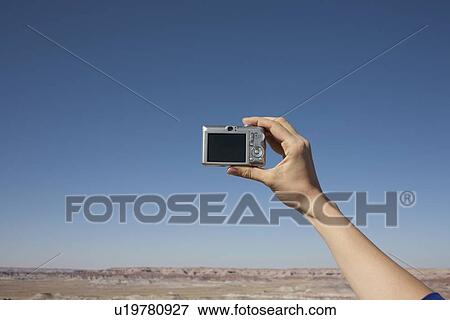 Hand of woman holding camera up against blue sky View Large Photo Image Stock Photo - Hand of woman holding camera up against blue sky. Fotosearch