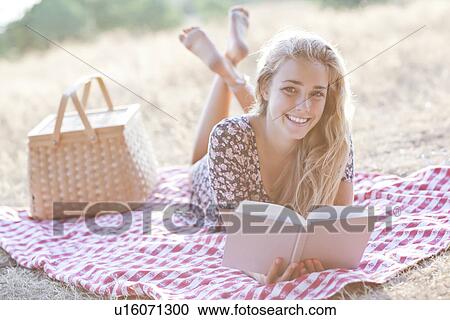 Stock Image - Happy teenage girl (16-17) reading book outdoors. Fotosearch