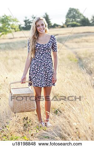 Stock Photo - Happy teenage girl (16-17) standing in meadow, holding picnic basket. Fotosearch